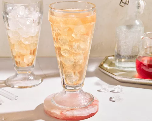 Two parfait glasses of old-fashioned cream soda on ice shown with a bottle of soda and a pitcher of strawberry simple syrup